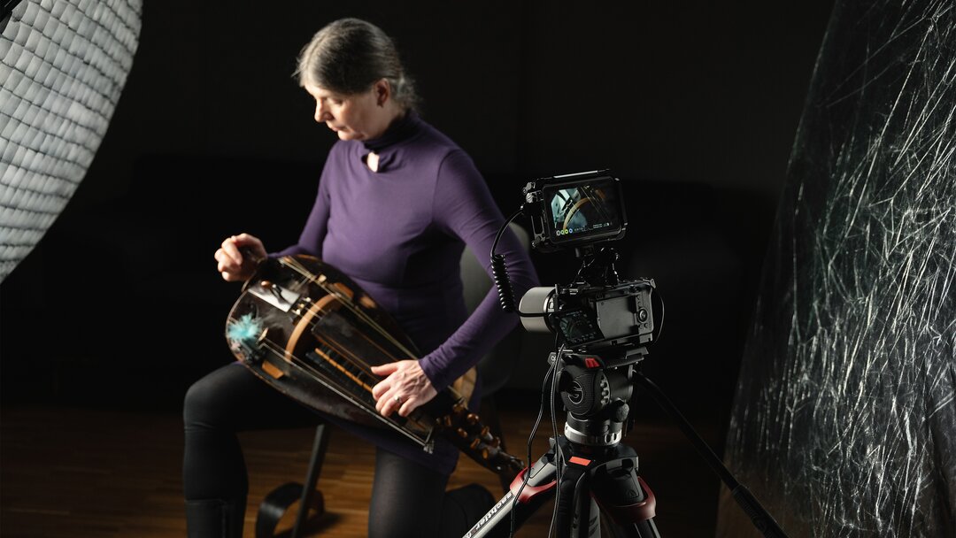 A photo of a woman being filmed playing a hurdy-gurdy